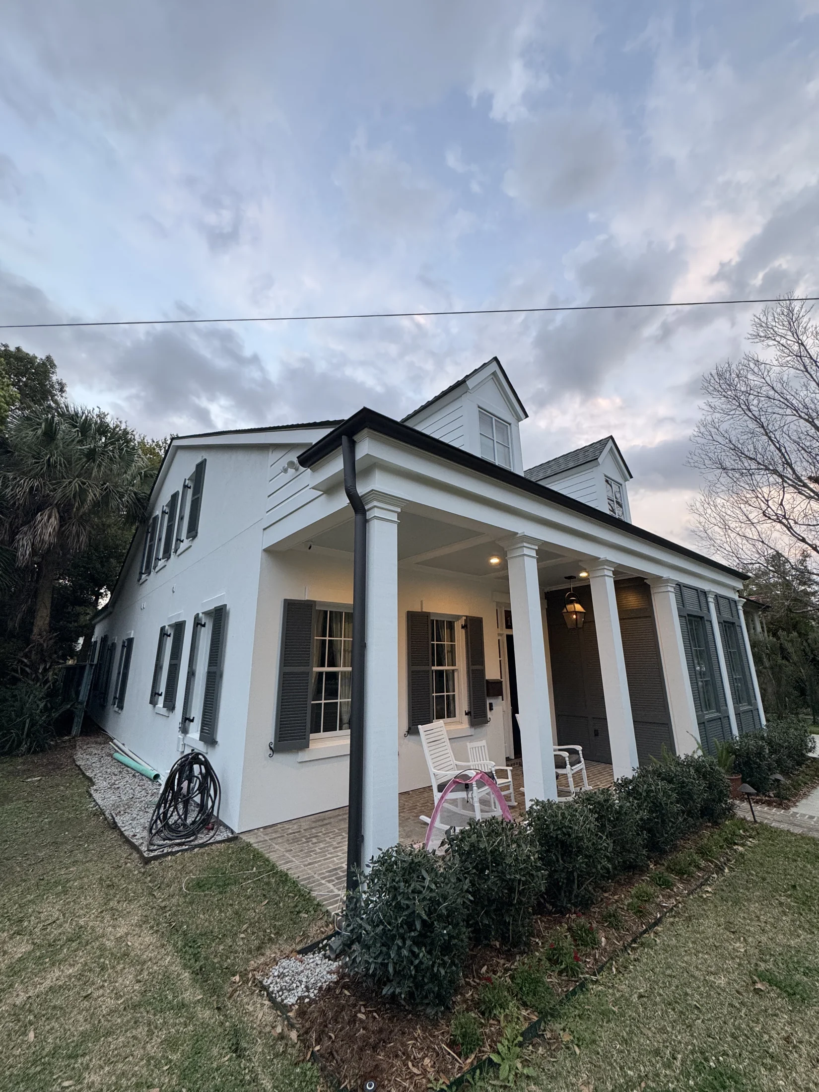 Freshly painted two-story white stucco home with dark gray shutters and covered columned porch in New Orleans