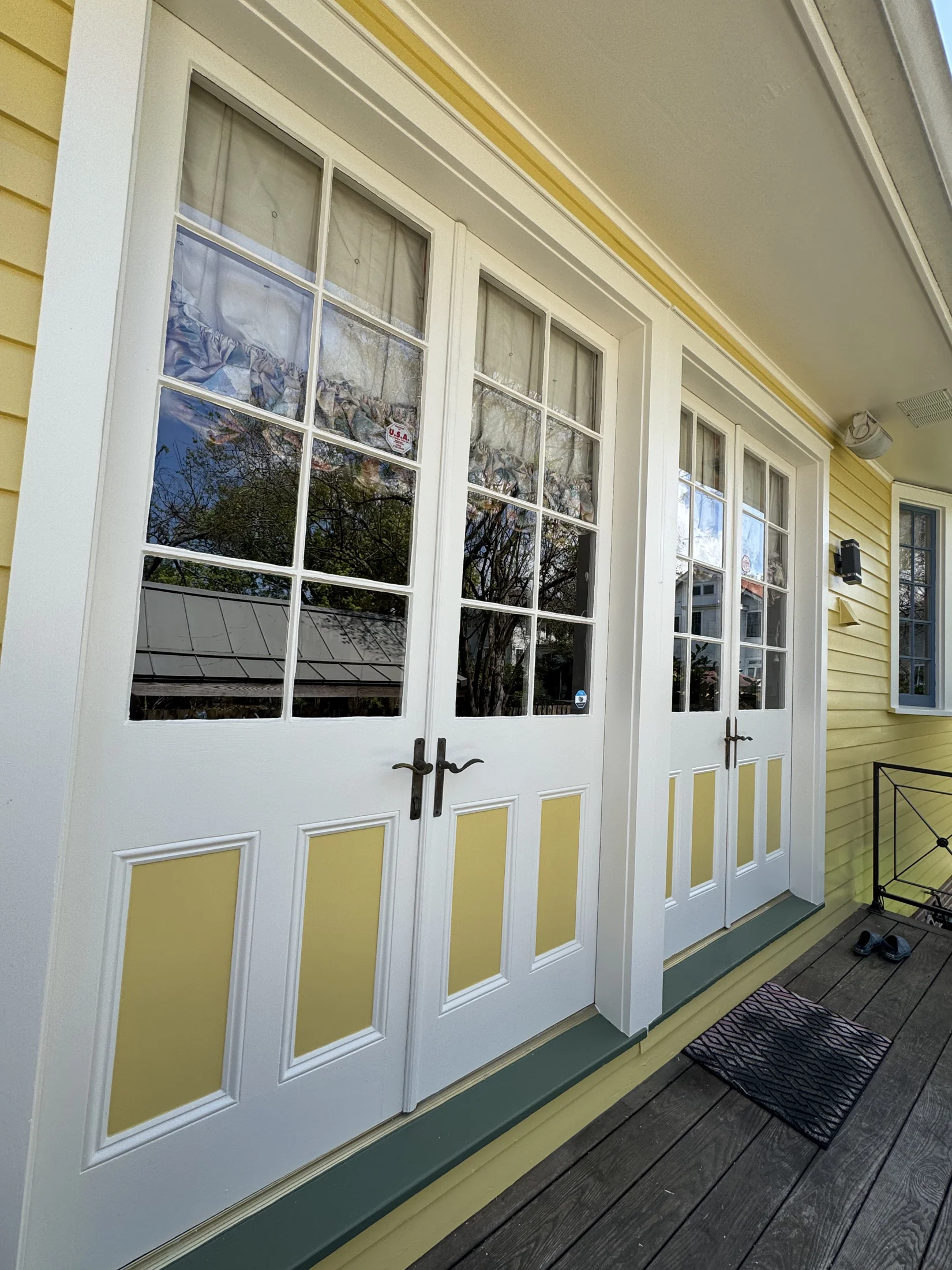 Newly painted white French doors with yellow lap siding on a New Orleans shotgun home porch